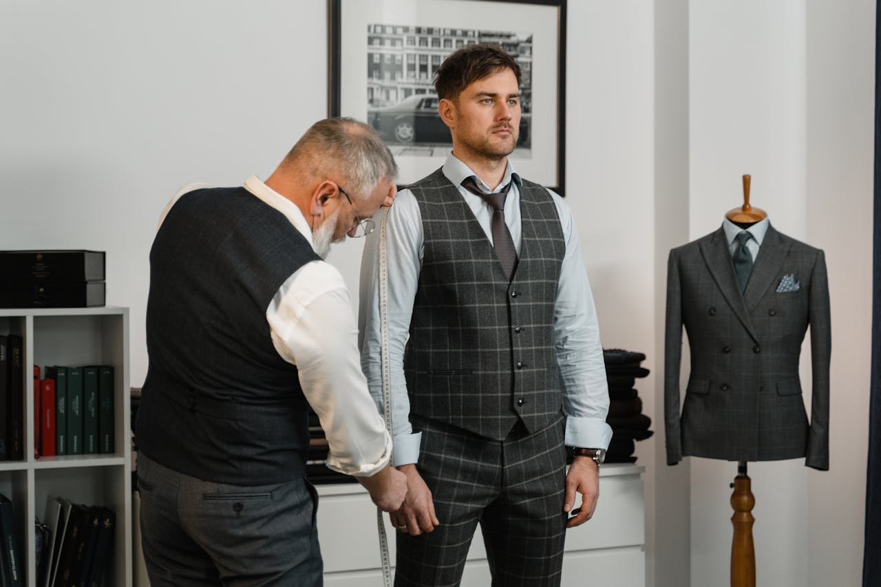 about-img-01 A professional tailor takes measurements of a client for a custom tailored suit in a stylish atelier.